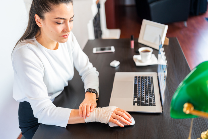 Business woman with bandaged wristis suffering from wrist joint pain at home office. Office syndrome hand pain by occupational disease.